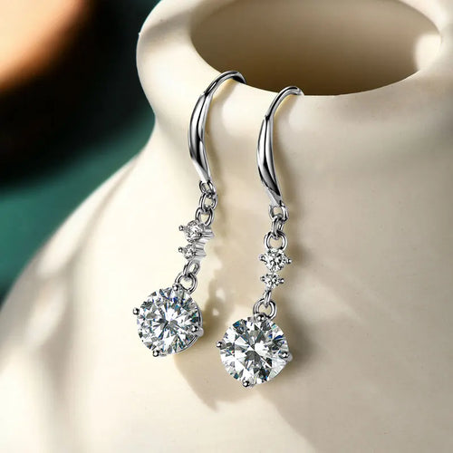 Women's silver dangle hook earrings with brilliant round moissanite stones on a cream background