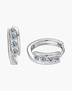 Two women's silver huggie hoop earrings with five round brilliant-cut moissanite stones each