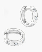 Two women's silver huggie hoop earrings with three bezel-set clear stones each