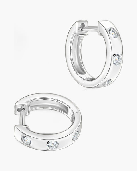 Two women's silver huggie hoop earrings with three bezel-set clear stones each