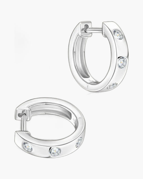 Two women's silver huggie hoop earrings with three bezel-set clear stones each
