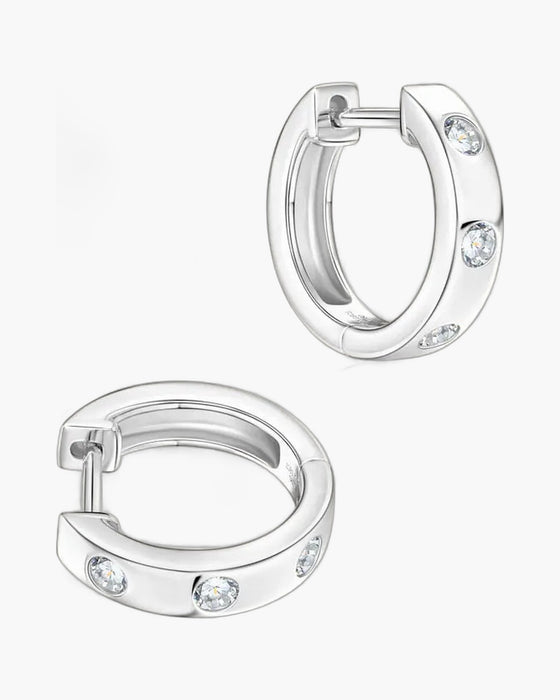 Two women's silver huggie hoop earrings with three bezel-set clear stones each